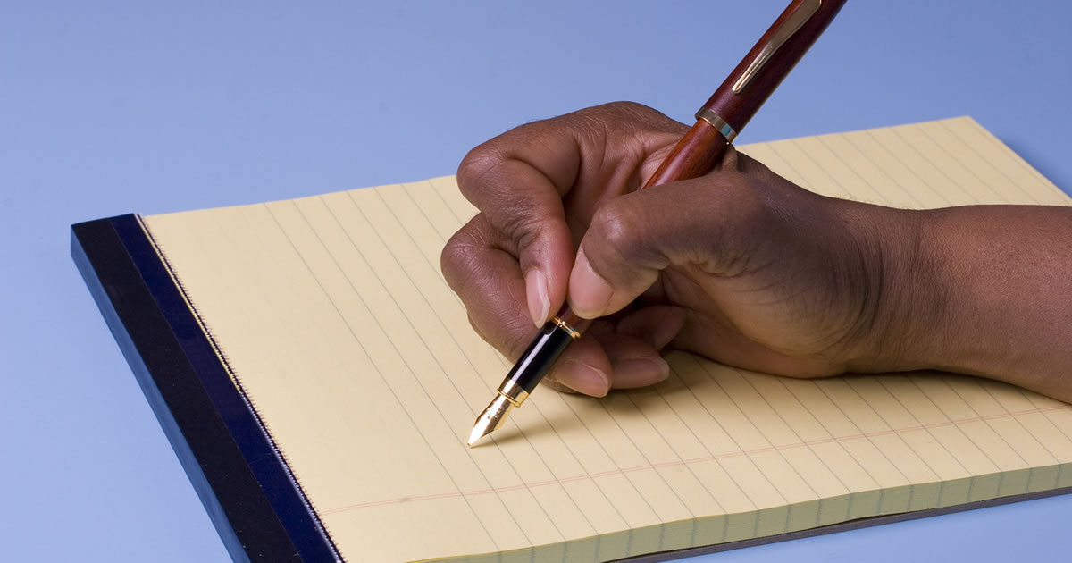 A hand holding a pen to a pad of paper