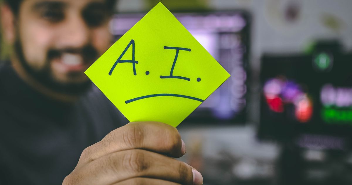 Smiling person holding up sticky note with A.I. written on it