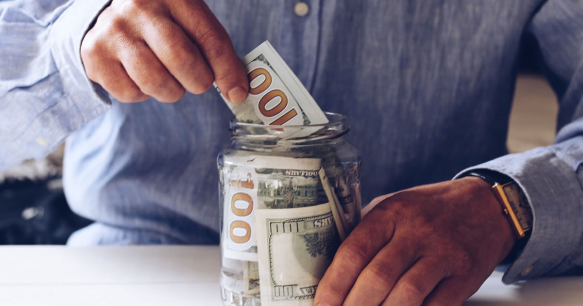 Man saving hundred-dollar bills in a clear jar