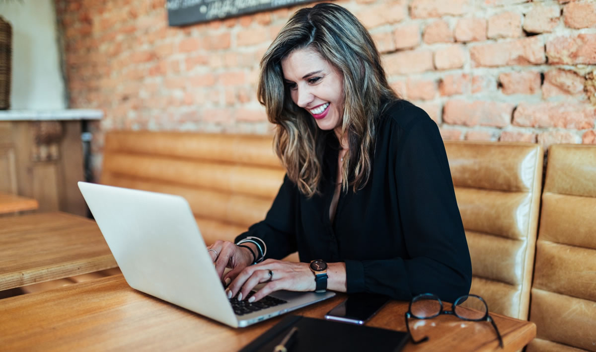 A smiling woman typing on a laptop computer at a table in a coffee shop