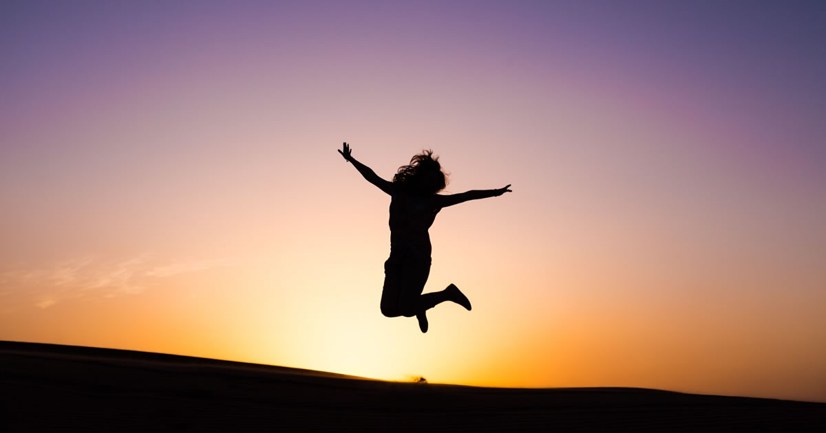 Silhouette of happy woman jumping for joy with colorful sunset