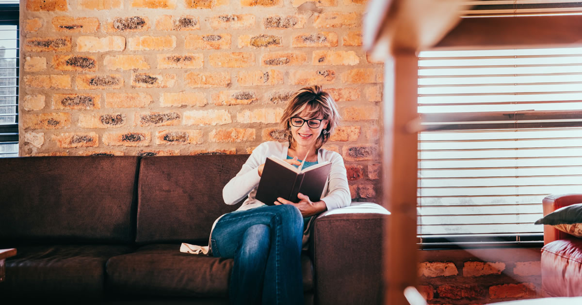 Smiling woman reading a book at home on couch in living room