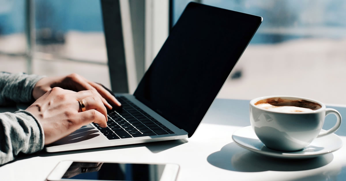 Writer typing on laptop with smartphone on table