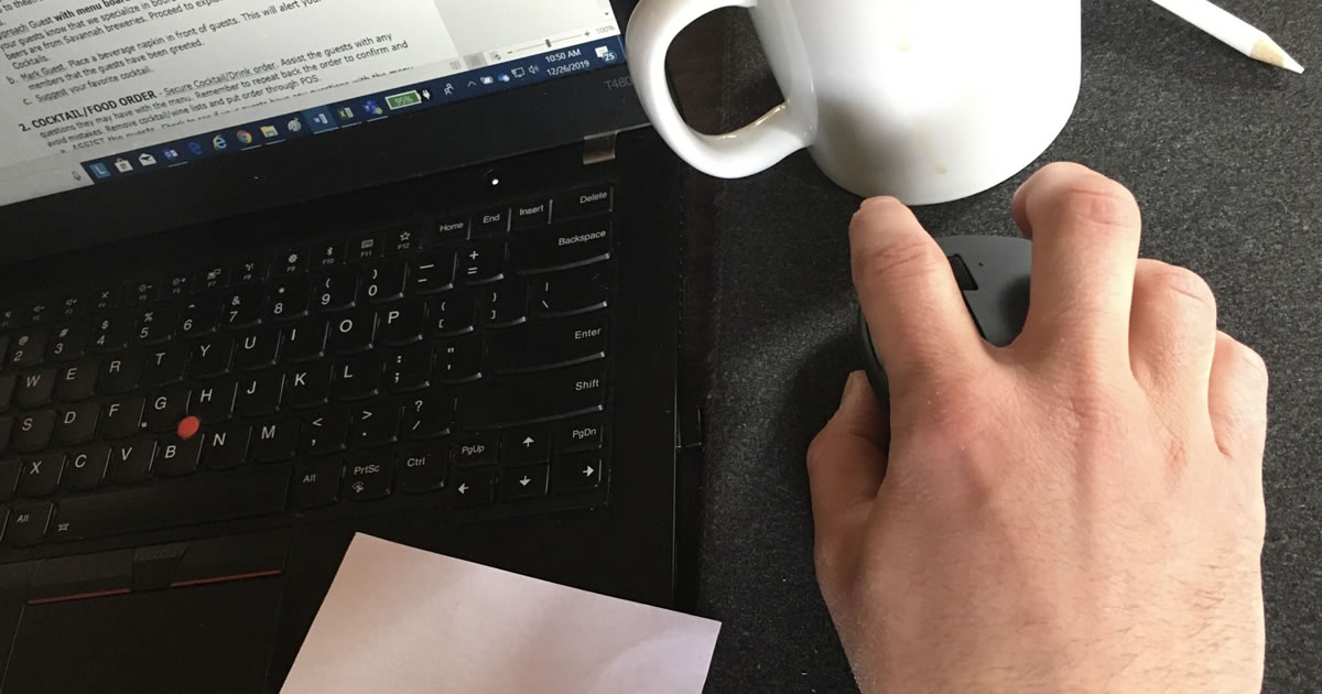 Closeup of desk with a man's hand on computer mouse next to laptop and coffee