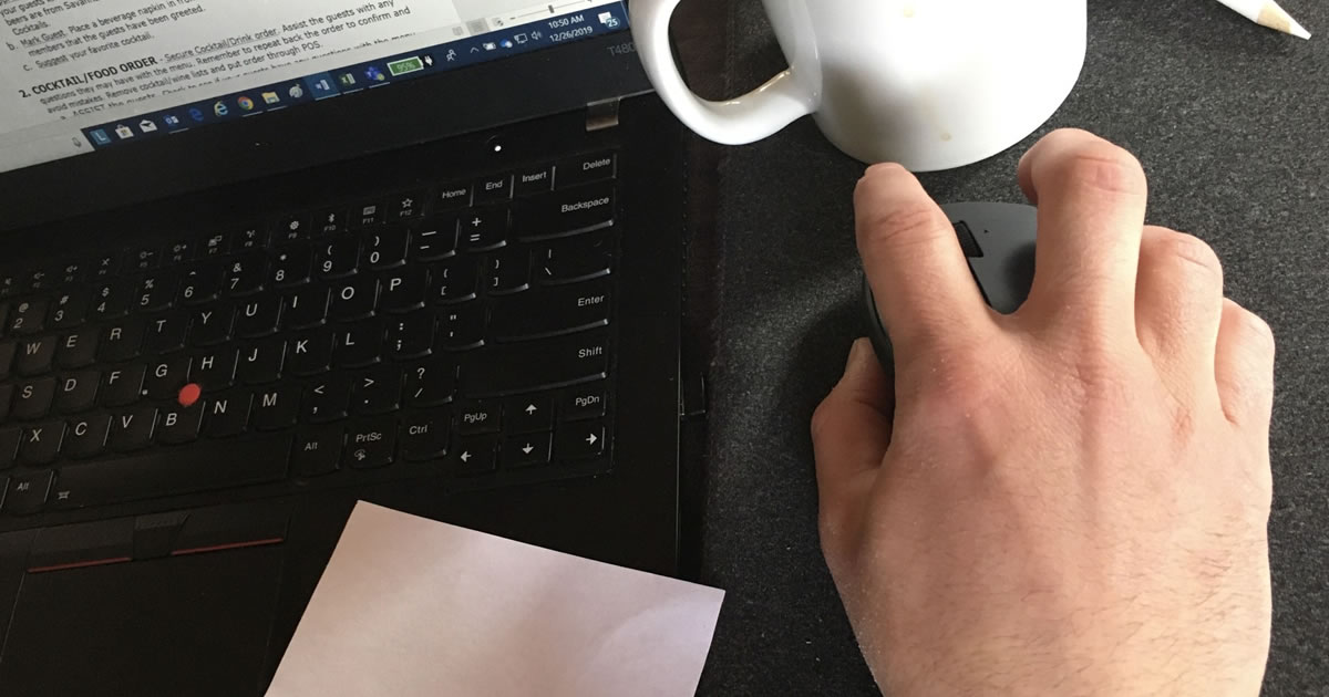 Closeup of desk with man's hand using computer mouse next to laptop and coffee