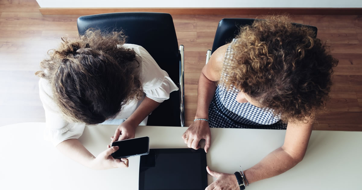 Overhead view of two businesswomen with smartphone and tablet working at office table together