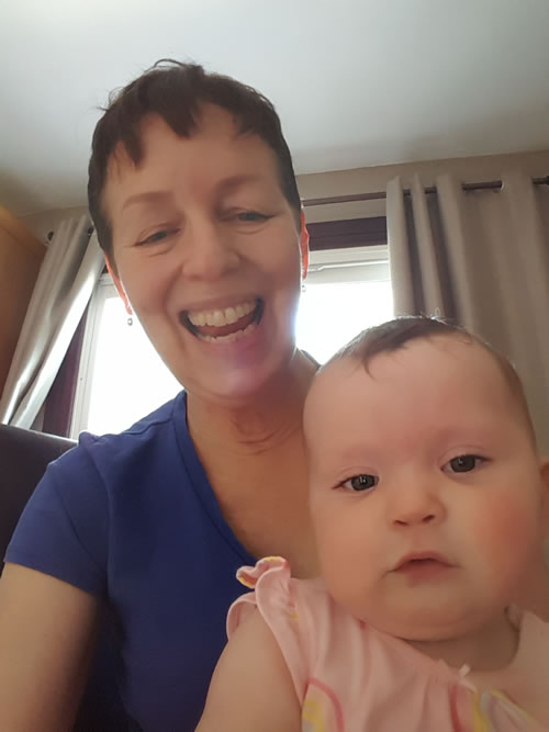 Photo of smiling closeup of writer Chris Allsop with her infant granddaughter