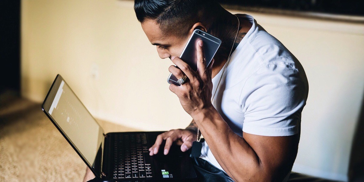 Man talking on smartphone while writing on laptop