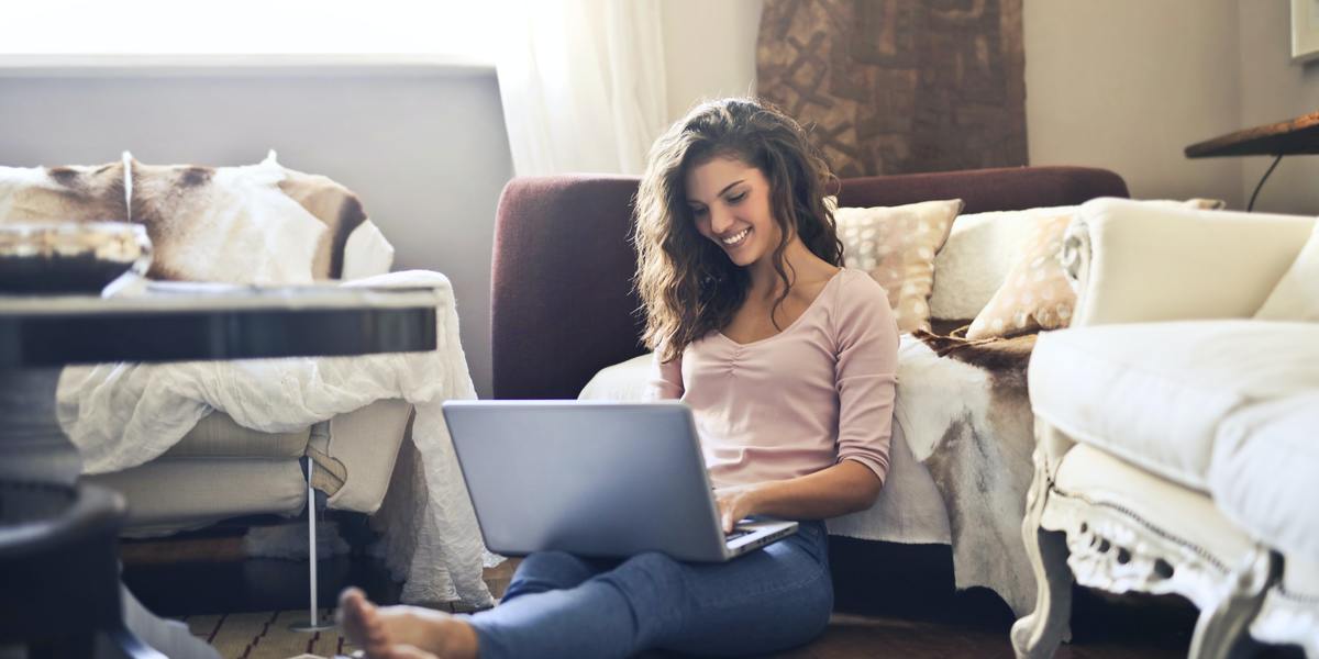 Young woman smiling writing on laptop sitting on the floor
