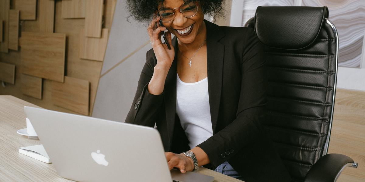African American smiling young woman writing on laptop and talking to a client over the phone