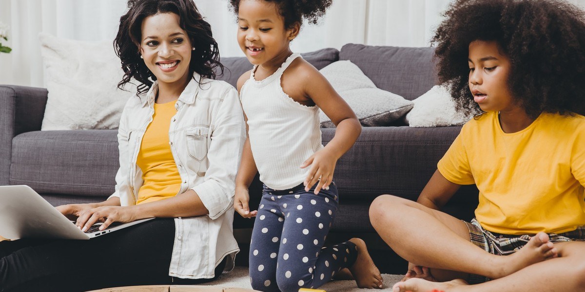 mother writing on laptop on the floor with children playing nearby