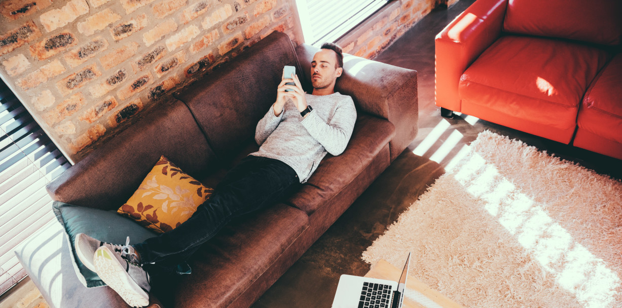 young male adult laying on couch browsing his mobile device