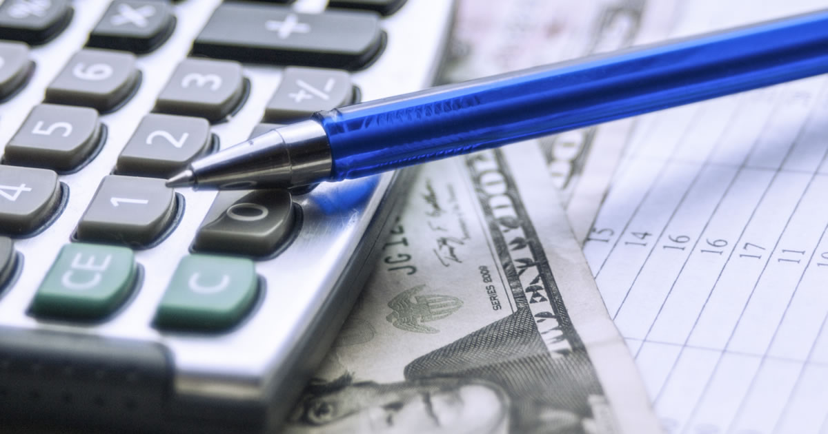 Closeup of pen resting on calculator, cash, and paperwork