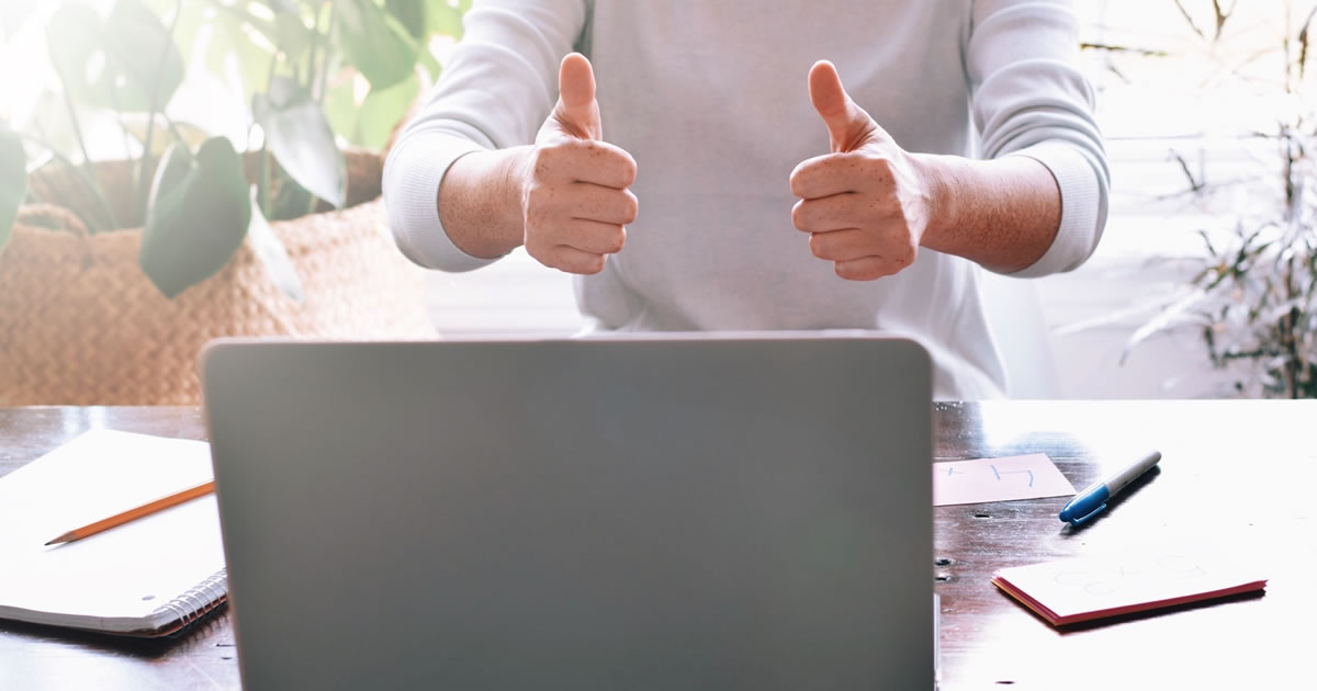 Person giving two thumbs up while sitting in front of laptop at coffee table