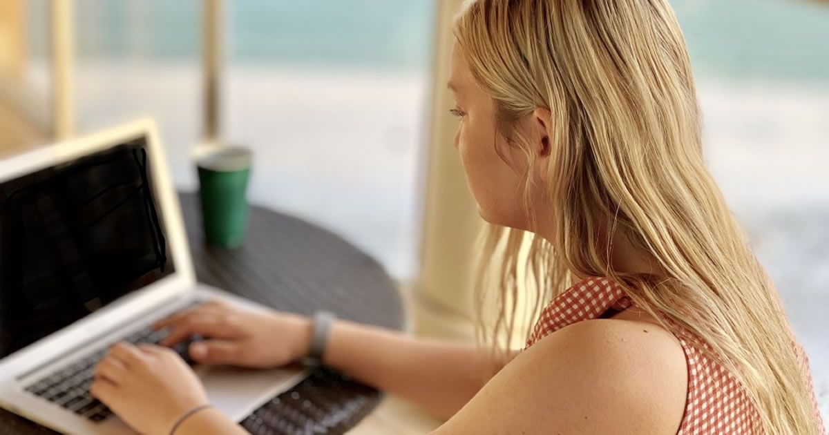 Young woman writing on laptop on balcony at beach