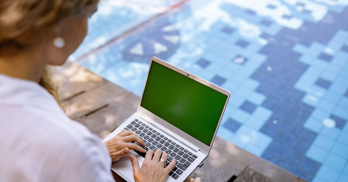 Female writing on laptop near swimming pool