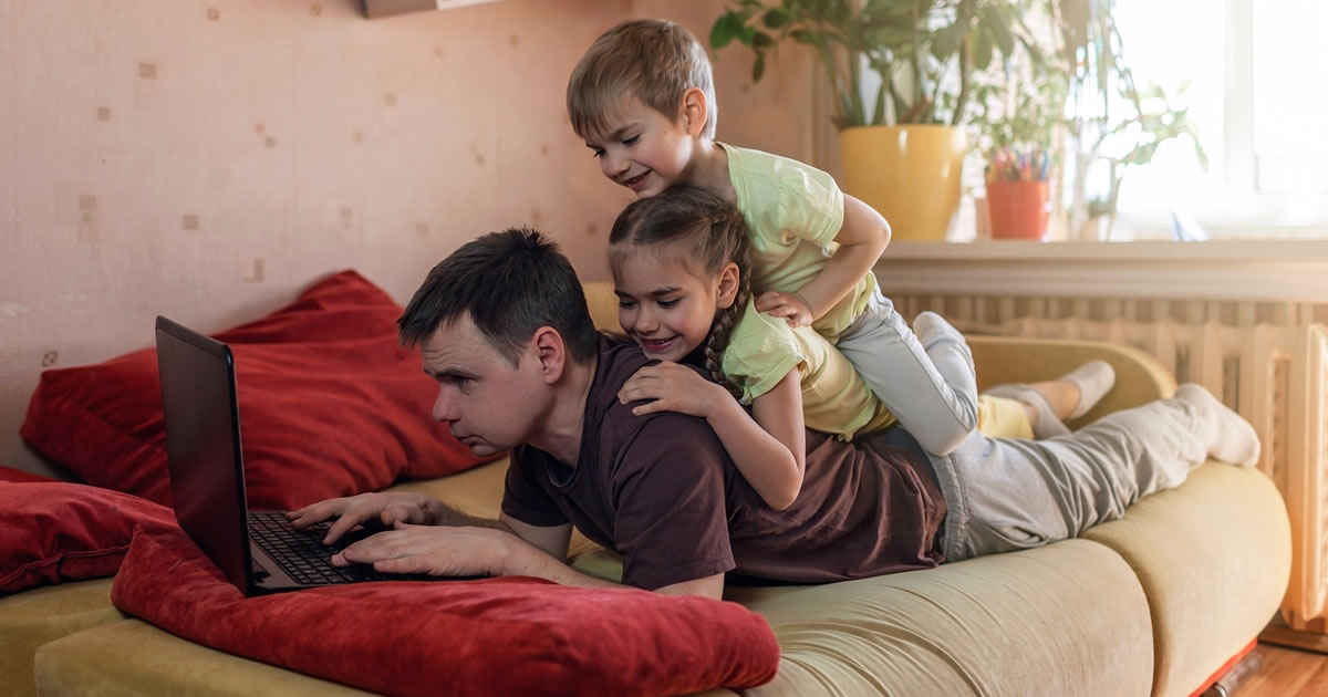 Happy man with children on his back writing on his laptop 