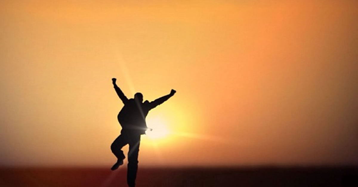 Silhouette of a businessperson with their arms up in celebration while facing the sun on the horizon