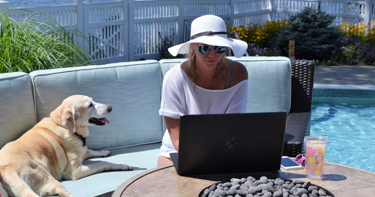 Woman writing on her laptop at the pool with her dog keeping her company