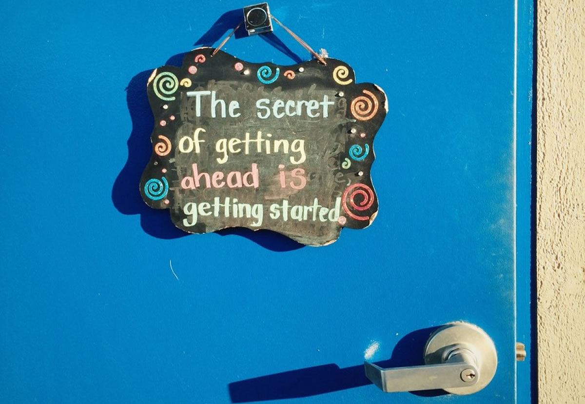 Blue door with colorful chalkboard sign displaying the words the secret of getting ahead is getting started