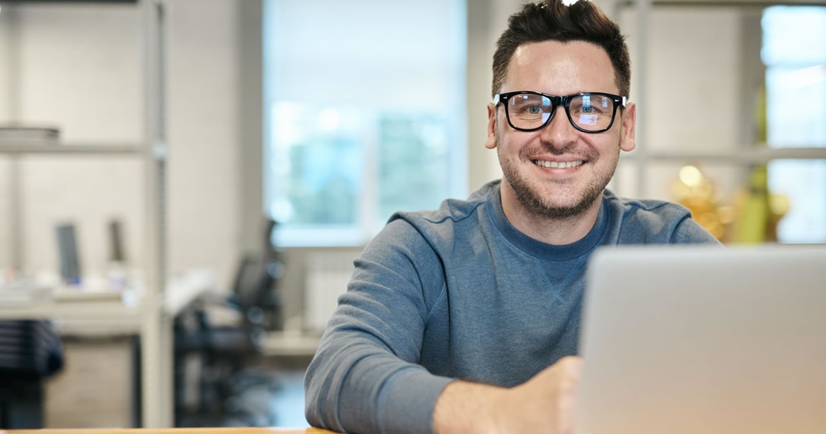 Smiling male writer sitting at table with laptop