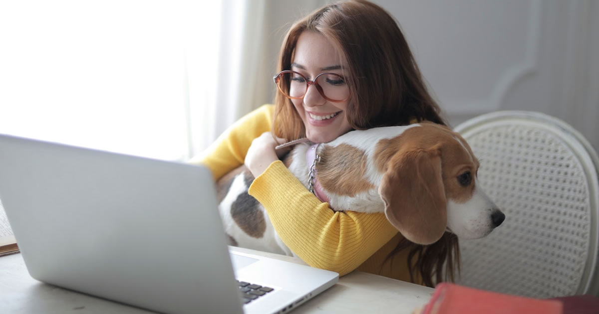 Woman working on laptop while smiling and holding a dog