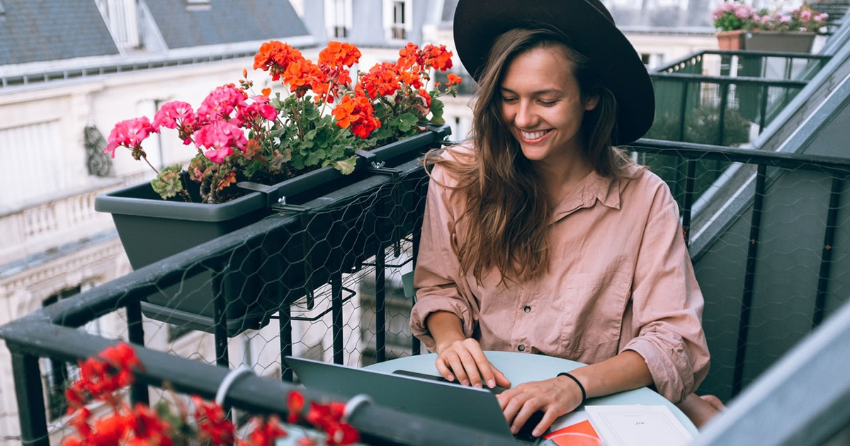 Woman writing on laptop on outdoor patio with flowers