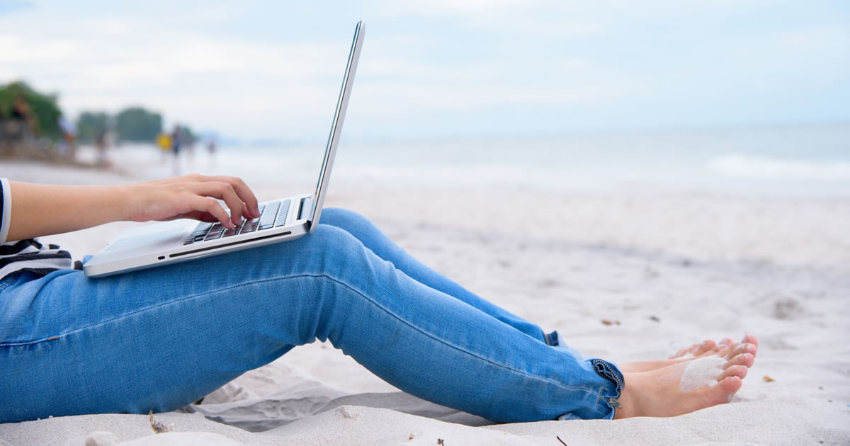 Freelance writer blogging on laptop on a sandy beach