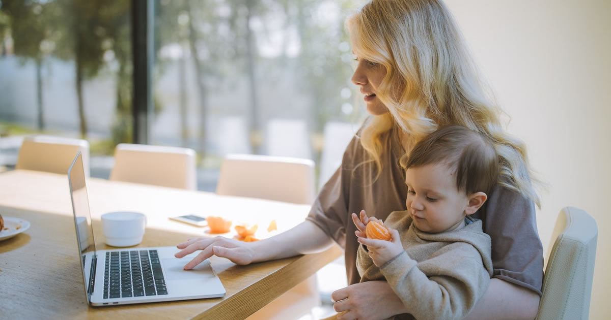 Woman writing on laptop with a baby on her lap
