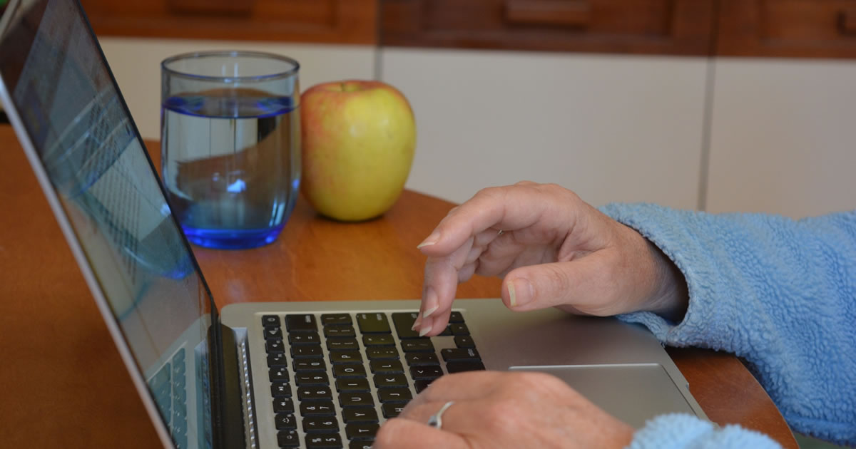 Woman writing on laptop computer, with an apple and a glass of water in the foreground