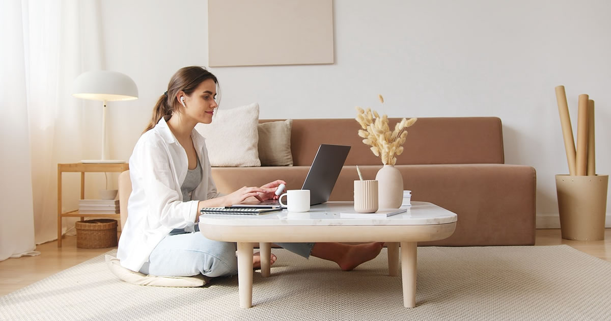 Happy woman sitting on living room floor while writing on laptop