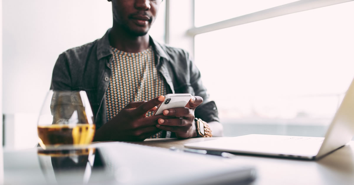 Man checking email on smartphone with laptop on table