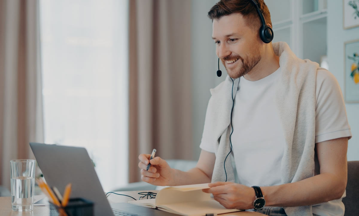 Male writer attending virtual event communicates online with other attendees using headphones with microphone