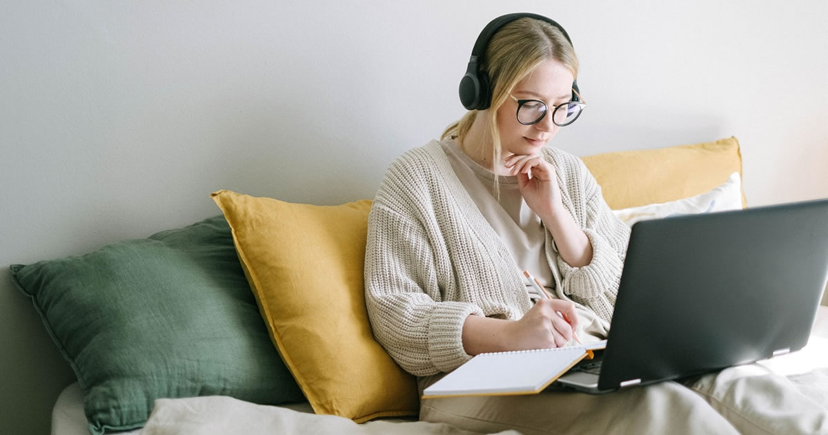 woman with laptop on her lap taking down notes