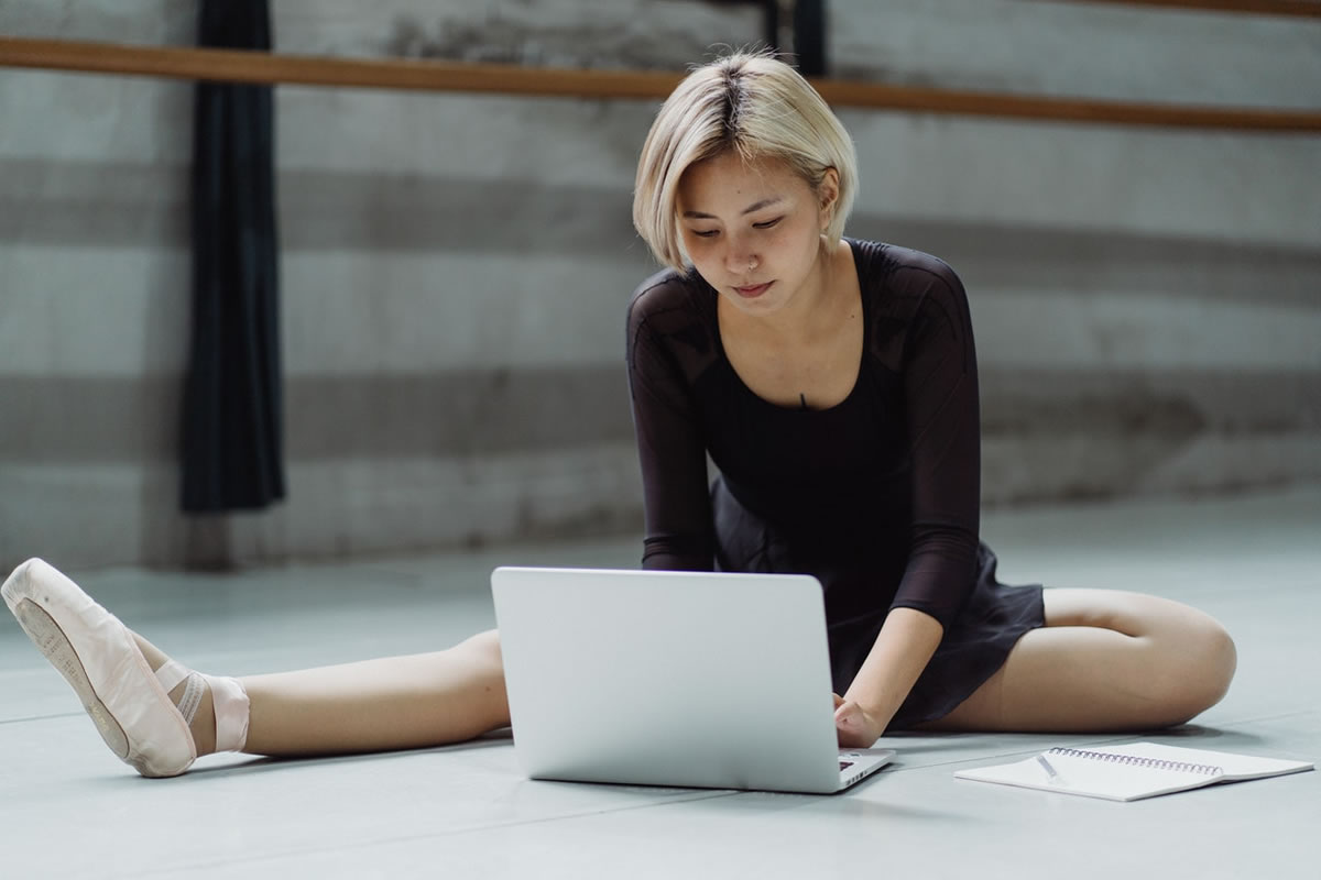 Ballet dancer sitting on floor of dance studio using laptop computer