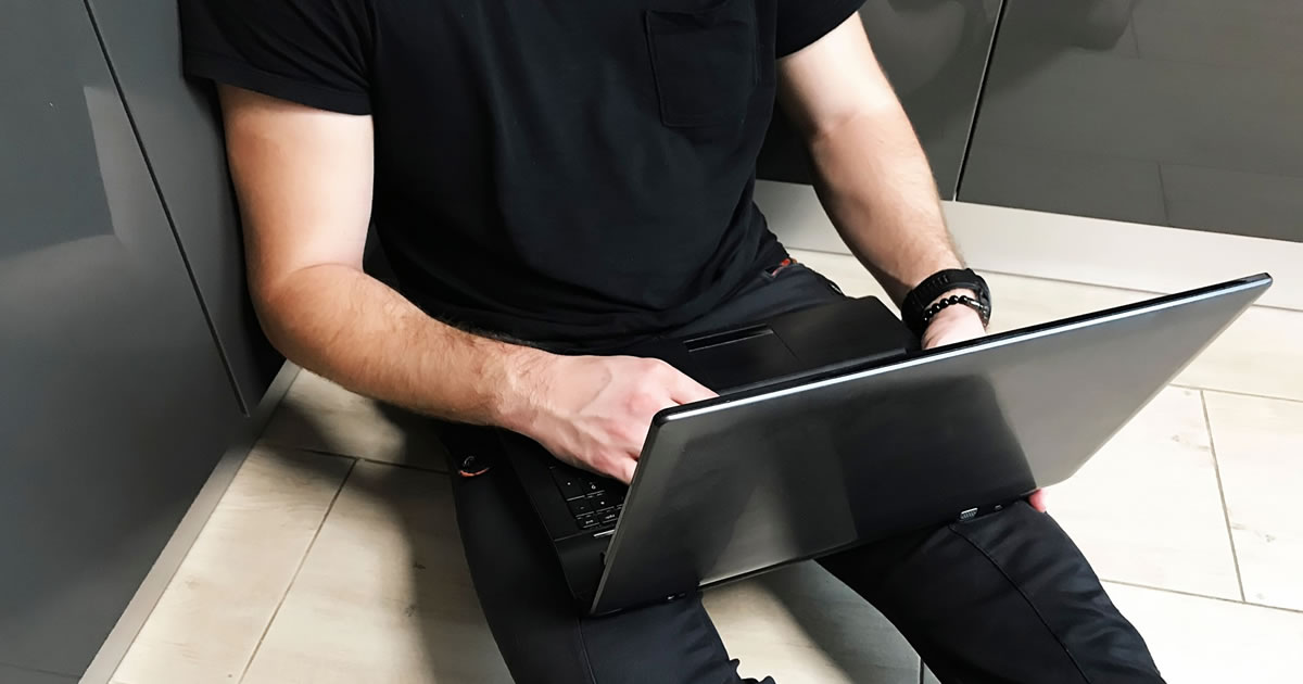 Young man writing on laptop, sitting on the floor, working from home