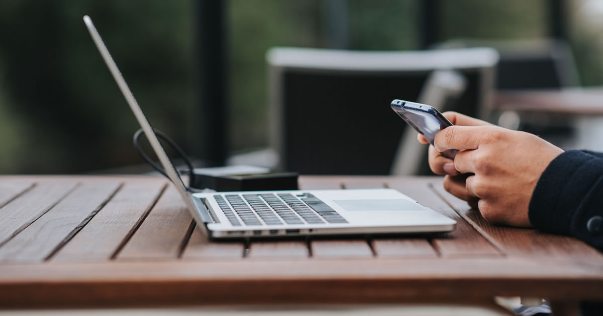 businessman text messaging on smartphone at table with laptop