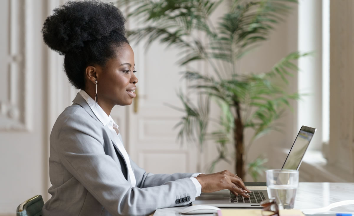 Smiling woman writing on laptop sitting at desk in home office