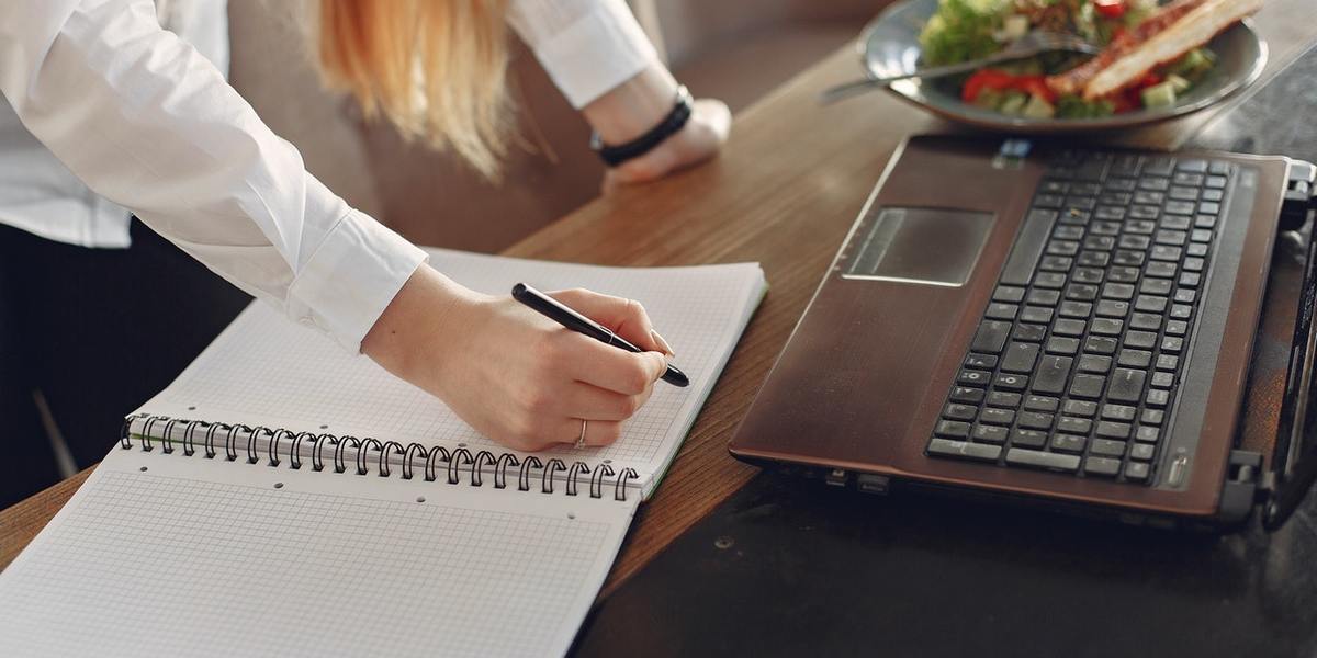 woman taking notes while reviewing laptop screen