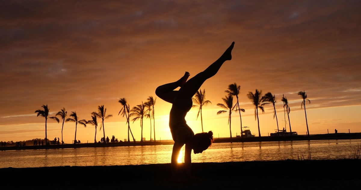 Silhouette of woman doing handstand on beach at sunset
