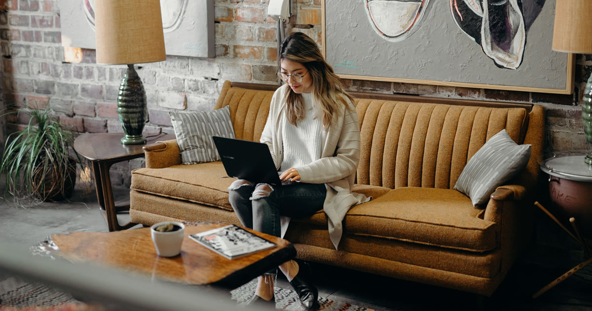 Smiling woman sitting on couch using laptop computer