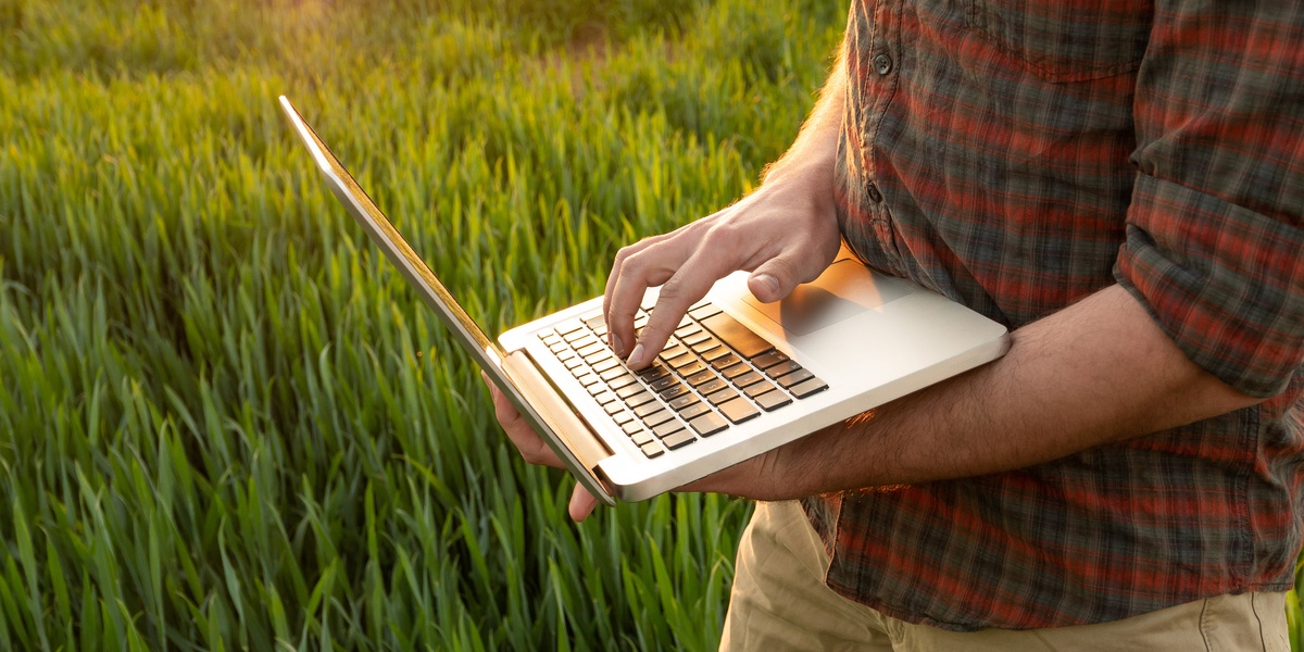 Young farmer using laptop walking in field.