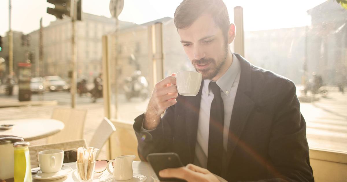 Writer holding a cup of coffee in a cafe looking at phone