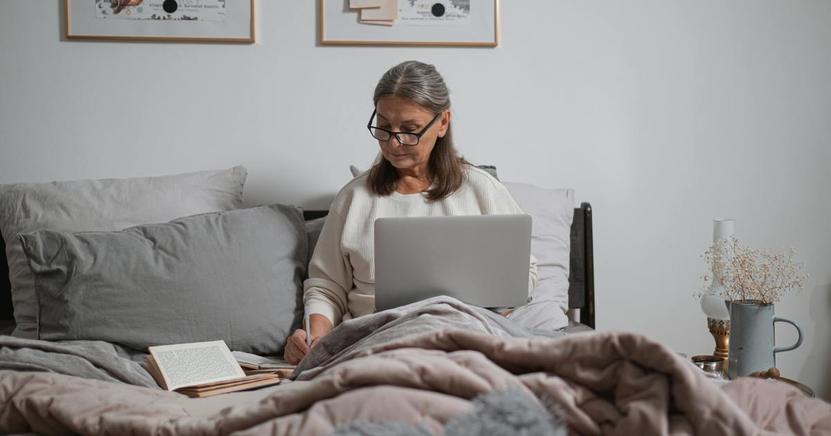 Writer sitting on bed typing on laptop