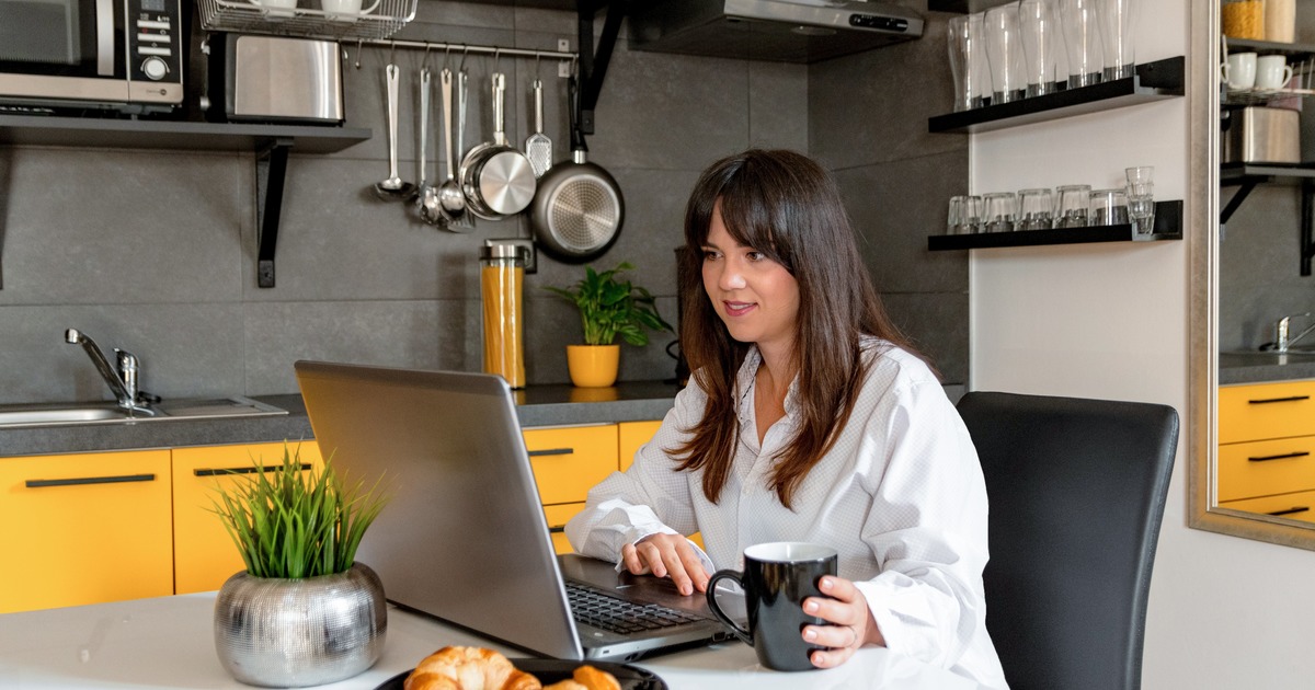 Writer sitting at kitchen table typing on laptop