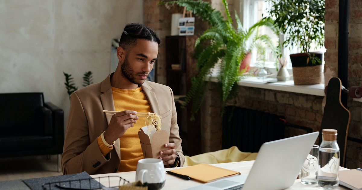 Writer eating noodles while looking at laptop