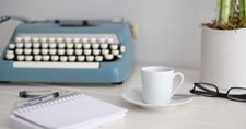 Typewriter, notepad, pen, cup and saucer, eyeglasses, and plant on a desk