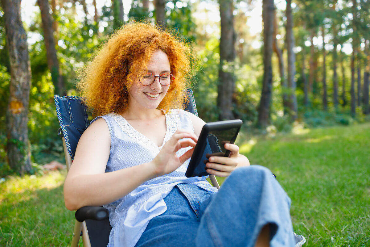 Female writer reading e-reader on a lawn chair outside